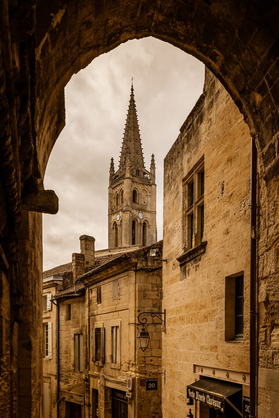 A view through a stone arch to a church spire in a warm old French town.