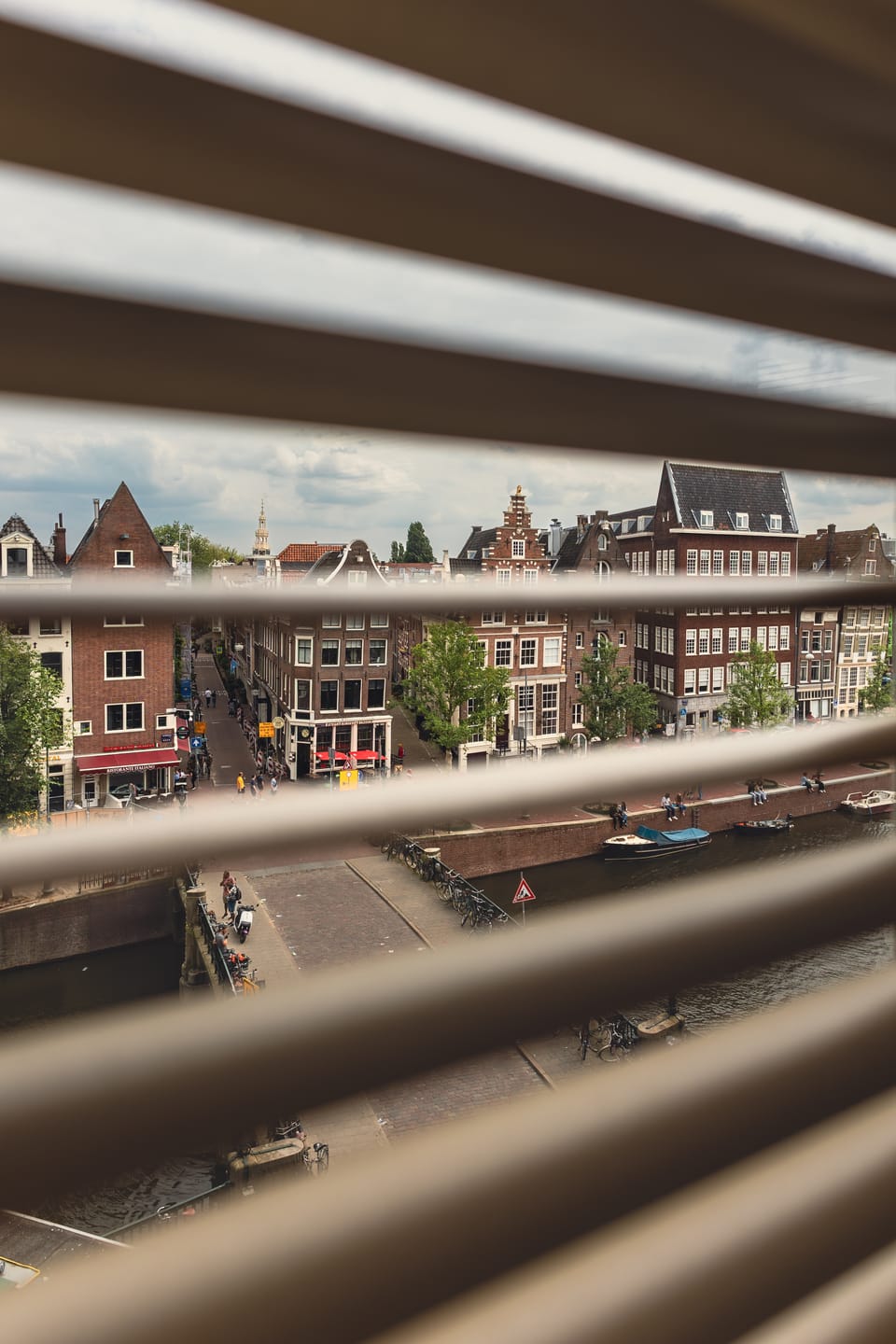An Amsterdam canal glimpsed through the slats of a window blind.