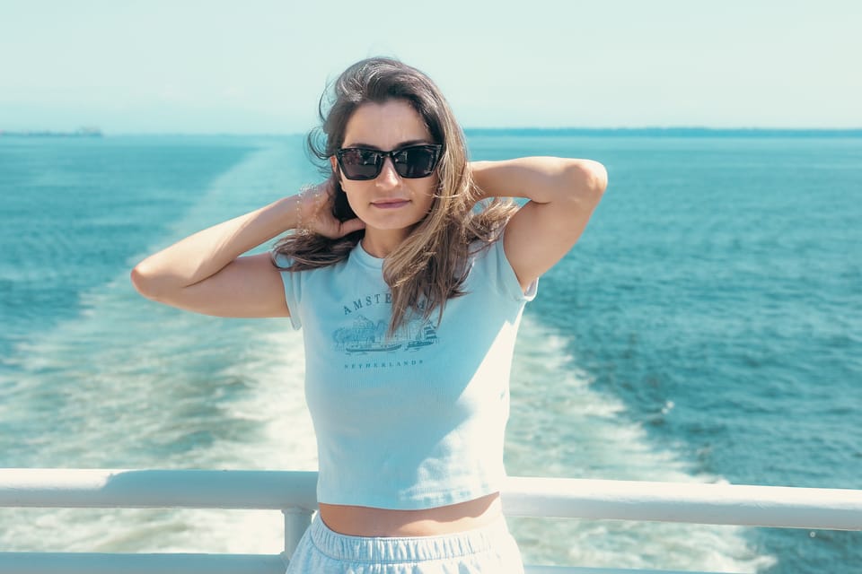 A woman in a white top and sunglasses on a ferry deck, her hair caught in the wind.