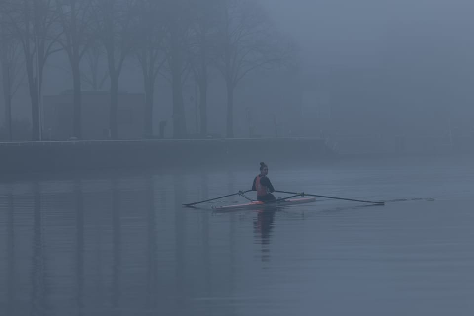 A lone rower gliding across still water through dense fog in Amsterdam.
