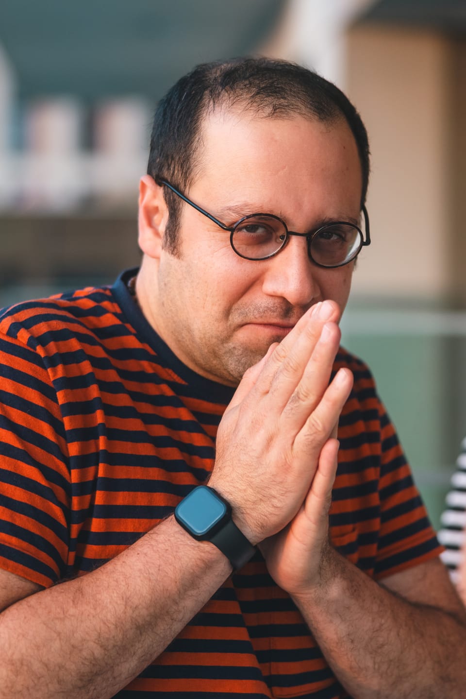 A candid portrait of a man in a striped shirt with his hands pressed together.