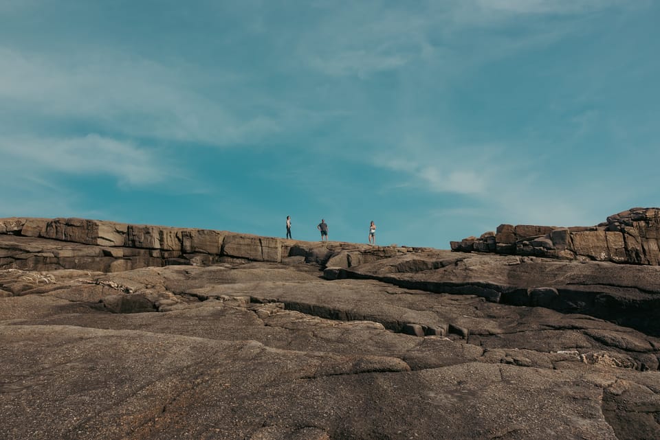 Tiny figures walking across a vast rocky headland above the Atlantic.
