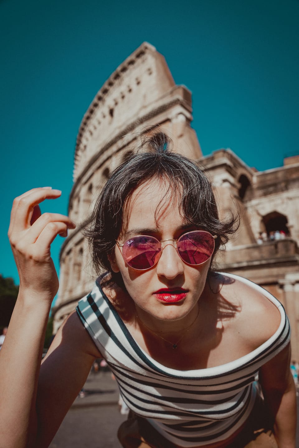 A playful portrait of a woman in red heart-shaped sunglasses before an ochre facade.