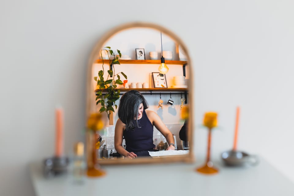 A woman working in a kitchen reflected in a round mirror among warm candles.