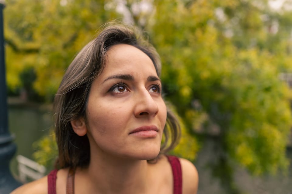 A portrait of a woman in golden light framed by soft green foliage.