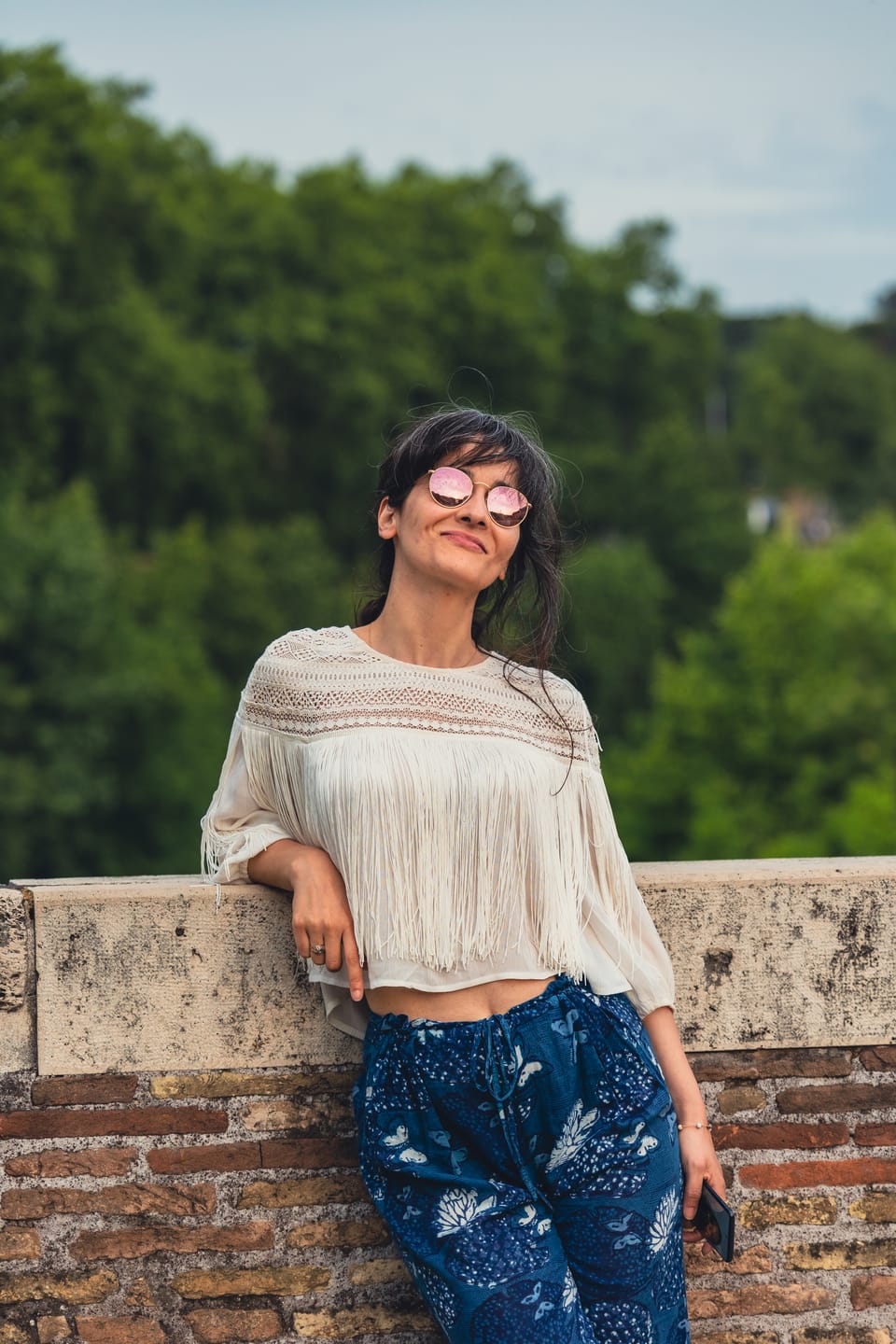 A woman in a white blouse leaning on a stone bridge wall at dusk.