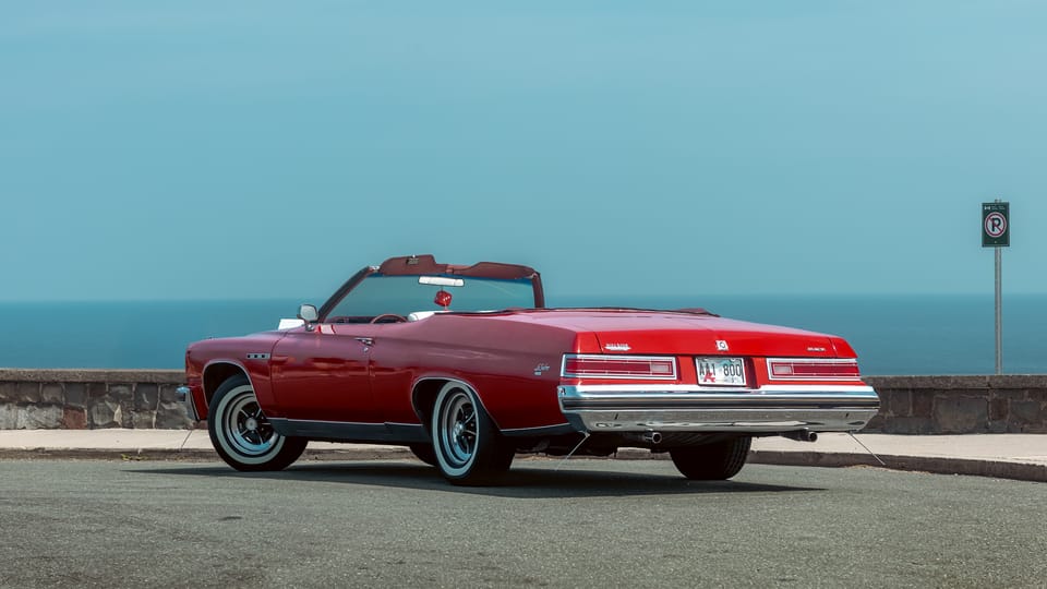 A vintage red convertible parked along an empty seafront road.