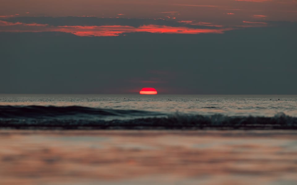 A red sunset over a calm sea with the waves smoothed into mist.