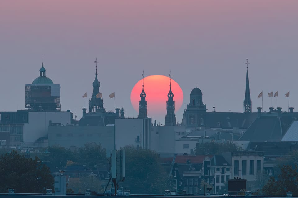 A deep red sun setting behind the spired silhouette of the Amsterdam skyline.