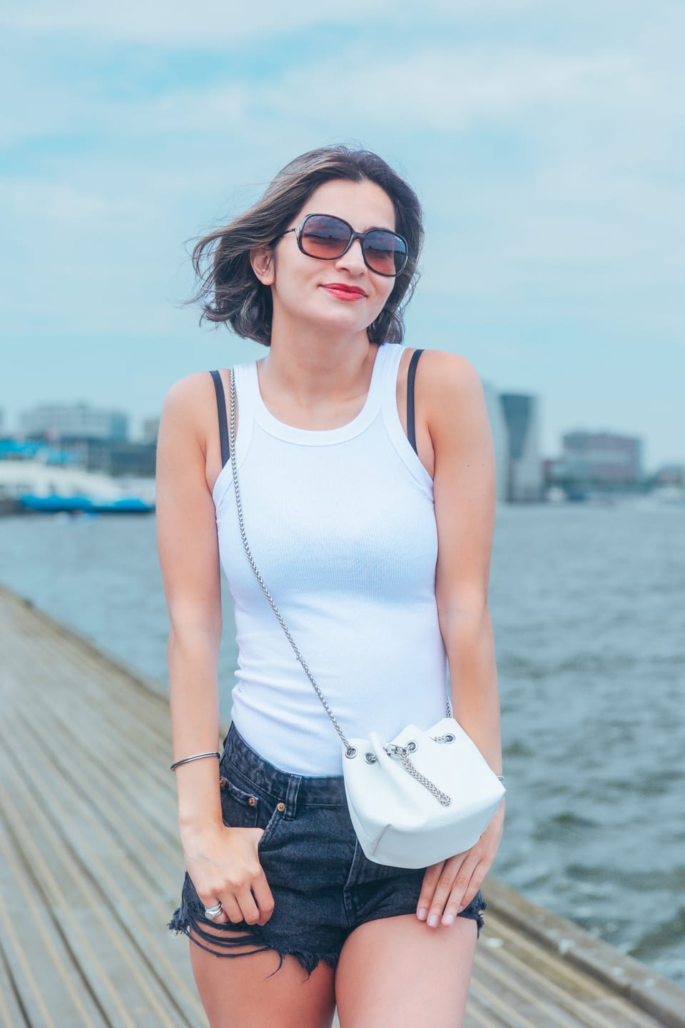 A woman in a white top walking a wooden pier with the harbour behind her.