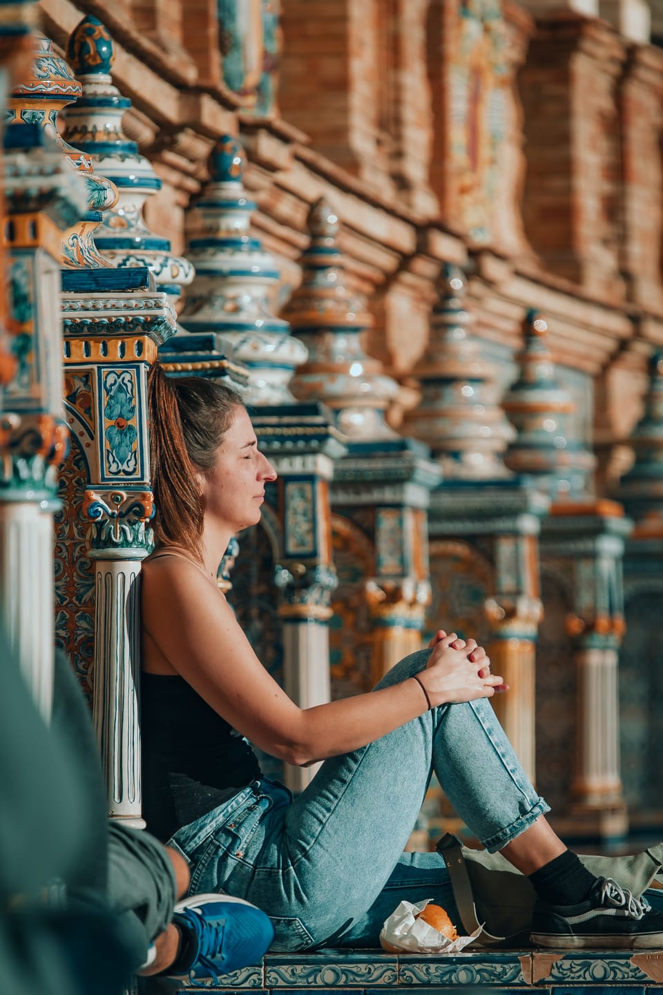 A woman sitting among the ornate tiled columns of a grand plaza.