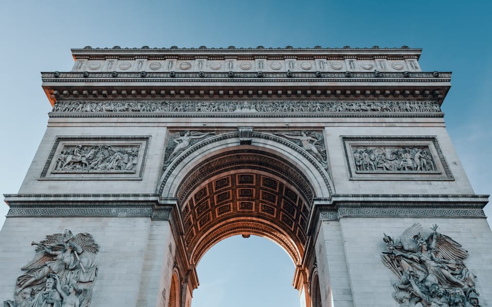 The Arc de Triomphe seen from directly below against a blue sky.